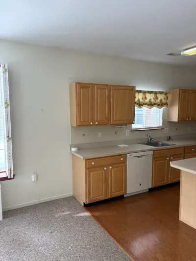 An outdated kitchen with oak cabinets, laminate counters, and a carpet-to-laminate flooring transition before renovation.