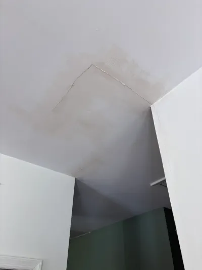 Close-up of a ceiling corner showing water staining and a cracked drywall seam near a doorway.