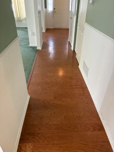 Hallway with wood-look flooring, green wainscoted walls, and a view toward the front door.