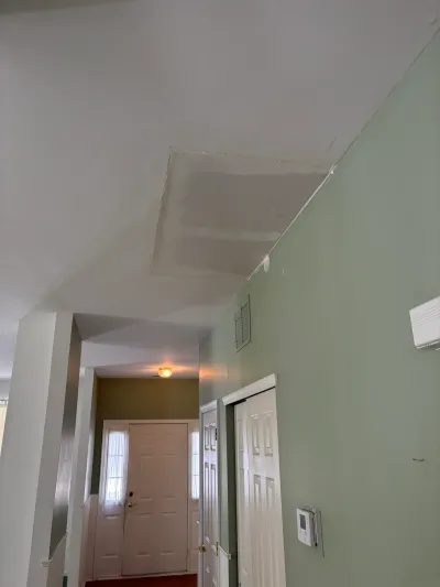 A sloped hallway ceiling shows an unfinished drywall patch above a green-walled entryway with a paneled front door.