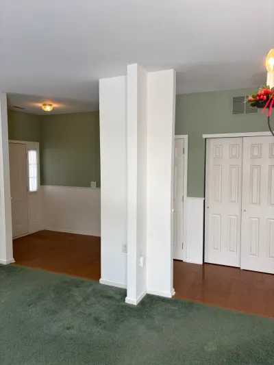 Empty room with green carpet transitioning to hardwood floors, sage green walls, and white wainscoting.