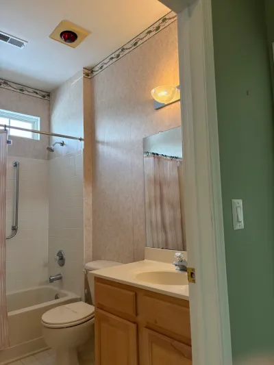 Dated bathroom with floral wallpaper border, tub/shower combo, and oak vanity awaiting renovation.