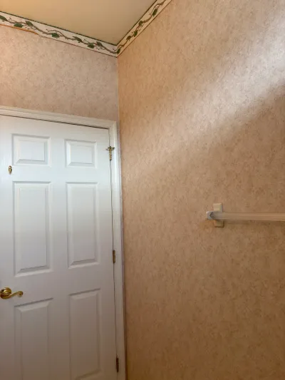 A hallway with tan wallpaper, a floral border, and a white paneled door with brass hardware before renovation.