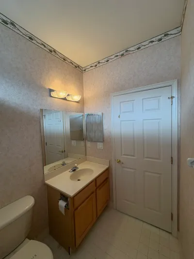 Dated bathroom vanity with oak cabinets, floral wallpaper, and a white paneled closet door before renovation.
