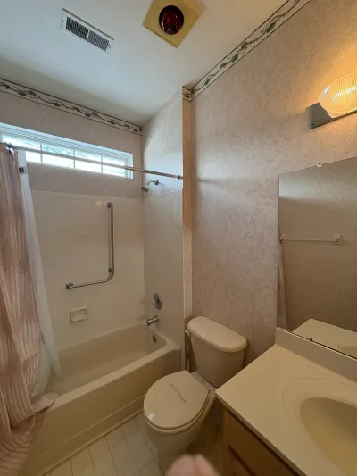 Dated bathroom with floral wallpaper, tile tub surround, and laminate vanity before renovation.