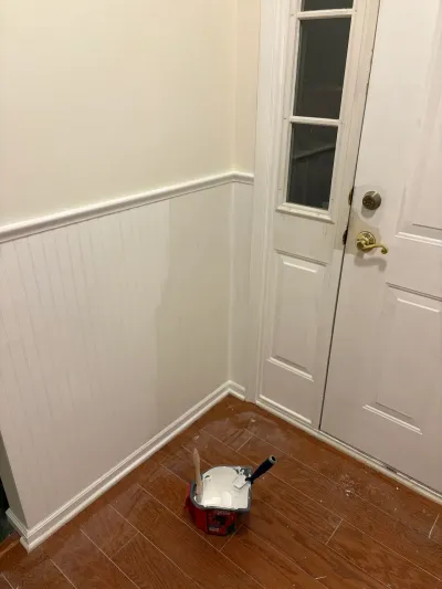 An entryway mid-painting with white beadboard wainscoting and a paint tray sitting on the floor near the front door.