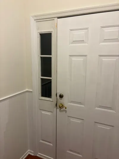 White paneled front door with a narrow glass sidelight and mismatched brass and bronze hardware.