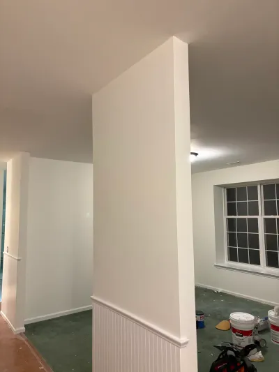 A basement mid-renovation with freshly painted walls, wainscoting trim, and paint supplies on a protected floor.