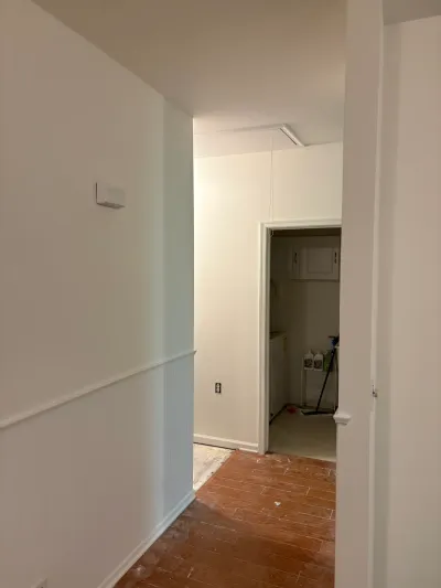 Hallway mid-renovation with wood-look tile flooring, white walls, and an unfinished ceiling light fixture.