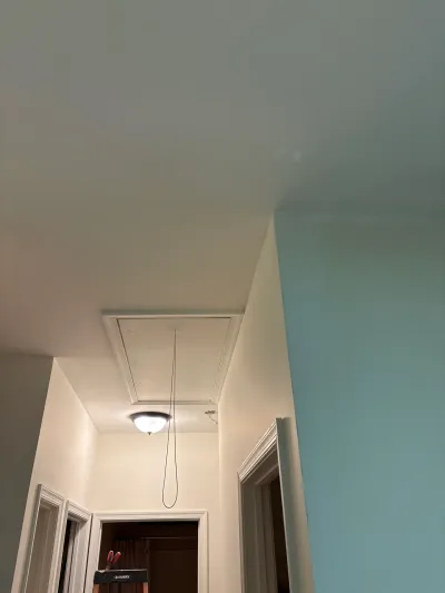 Hallway ceiling with an attic access hatch and pull cord, near a corner where white and teal walls meet.