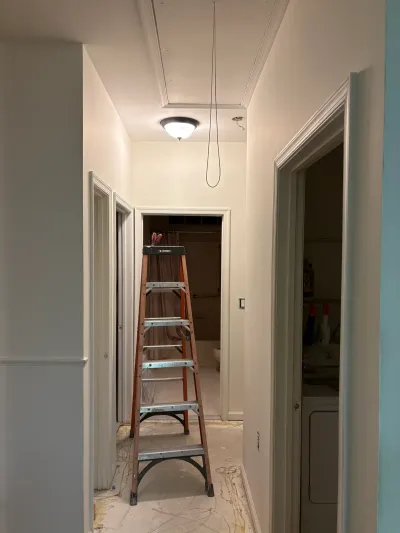 A hallway under renovation with exposed subfloor, a ladder, and views into an adjoining bathroom and laundry closet.
