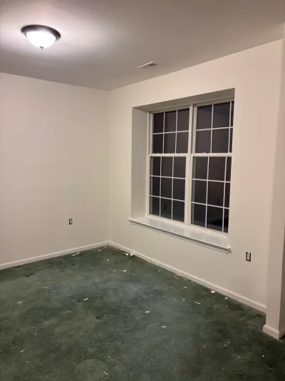 Empty room with dark green carpet, freshly painted white walls, and a recessed window at night.