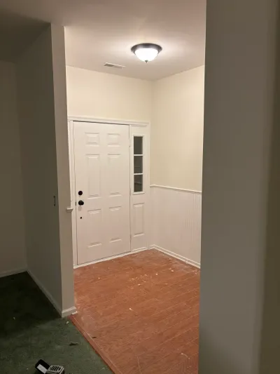 Entryway under renovation with exposed plywood subfloor, white beadboard walls, and a front door with sidelight.