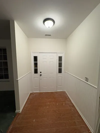 Foyer under renovation with a white front door, wainscoting, and wood-look tile floor scattered with debris.