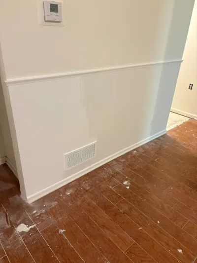 A hallway corner with new white wainscoting and paint-splattered wood flooring during a renovation.