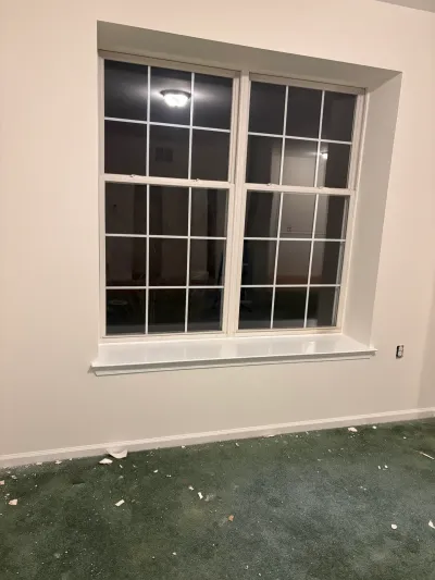A large paned window in a freshly painted room with green carpet and construction debris on the floor.