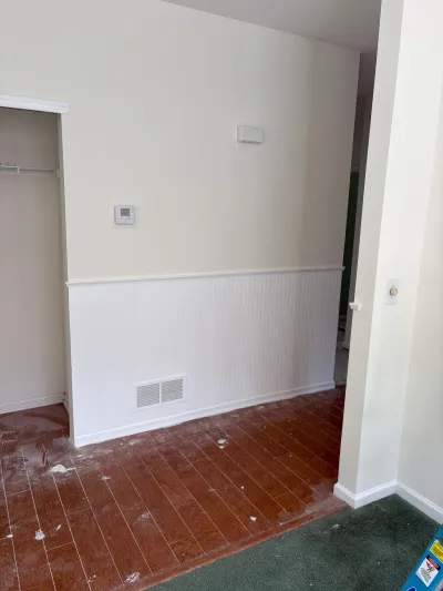 A room under renovation with beadboard wainscoting, paint-splattered wood flooring, and an open closet.