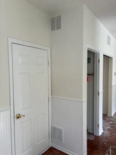 Hallway under renovation with beadboard wainscoting, a white paneled door, and an open closet showing an electrical panel.