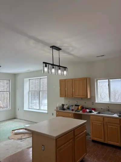 A kitchen mid-renovation with oak cabinets, an island, and an exposed subfloor in the adjoining room.