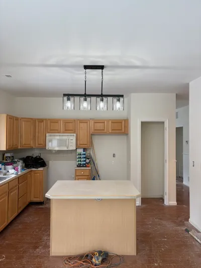 A kitchen mid-renovation with wood cabinets, a laminate island, and a new black pendant light fixture overhead.