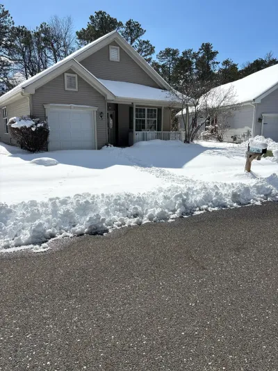 A gray house with a snow-covered roof and yard, attached garage, and a shoveled walkway to the porch.