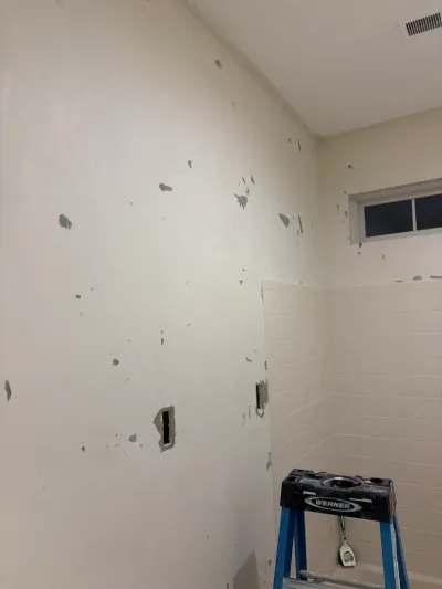 Bathroom wall under repair with patched drywall, tile wainscoting, and a step ladder in the corner.