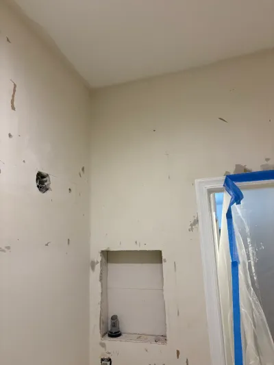 Bathroom wall mid-renovation with patched drywall, an exposed electrical box, and a taped-off window.