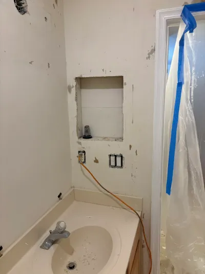 A bathroom vanity mid-renovation with exposed wiring, a wall niche, and a plastic dust barrier over the doorway.
