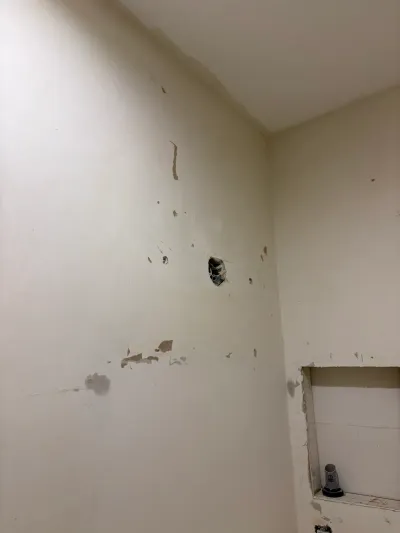 A bathroom wall with patched holes, an exposed outlet, and an unfinished recessed niche before renovation.