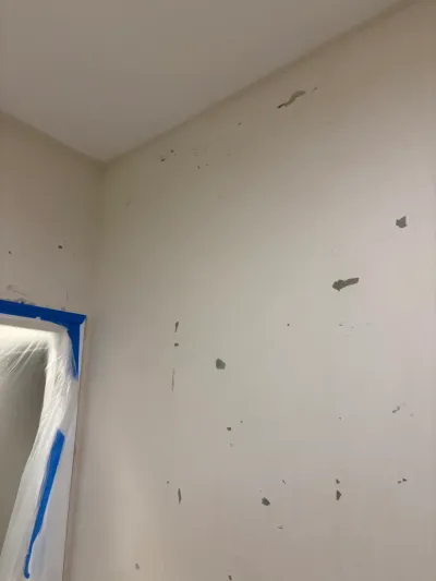 Interior wall with patched drywall repairs and a doorway taped off with plastic during renovation prep.