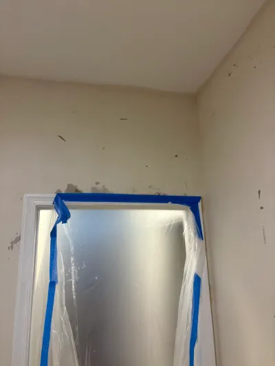 A taped-off doorway with plastic sheeting protects the opening during wall preparation work.