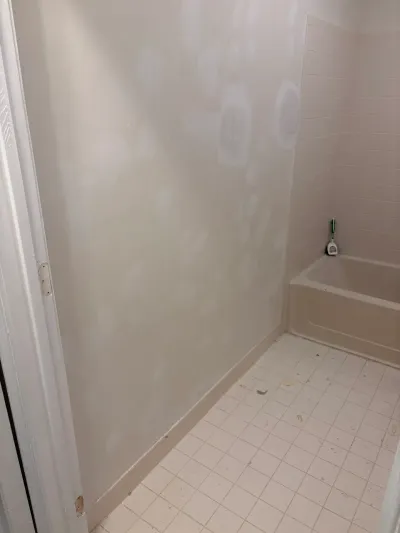 A bathroom before renovation with patched drywall, an alcove tub, and beige tile flooring.