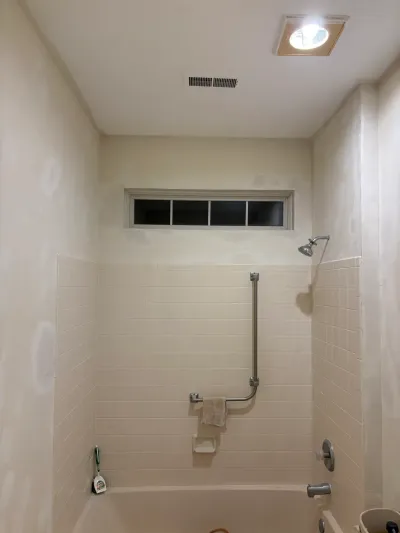 A tiled tub and shower alcove with exposed plumbing and unfinished patched drywall walls before renovation.