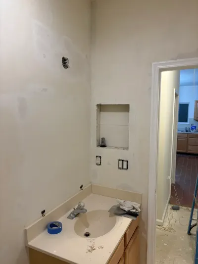A bathroom mid-renovation with patched drywall, a recessed wall niche, and an old vanity sink.