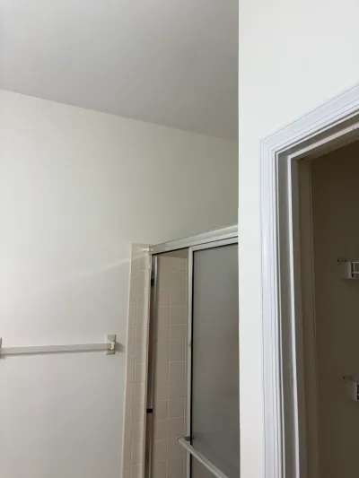 Corner of an outdated bathroom with a frosted glass shower door, beige tile, and a sloped ceiling.