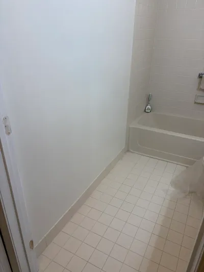 A dated bathroom with white tile tub surround and small square floor tile before renovation.