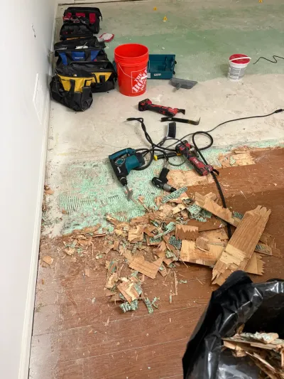 Flooring demolition in progress with tools, debris, and torn-up hardwood scattered across a subfloor.