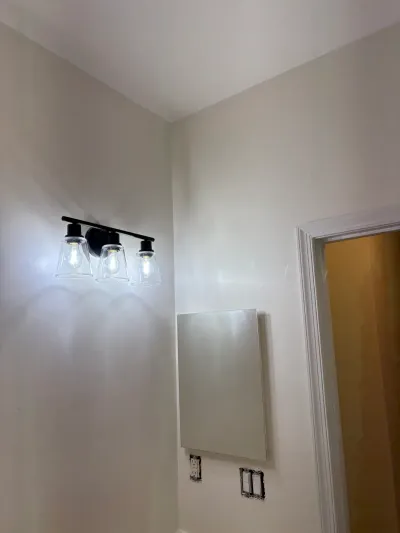 A bathroom mid-renovation with a black vanity light installed and an unfinished mirror cabinet on the wall.