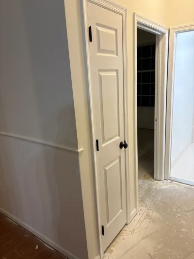 Hallway mid-renovation with a white paneled door, bronze hardware, and an exposed subfloor.