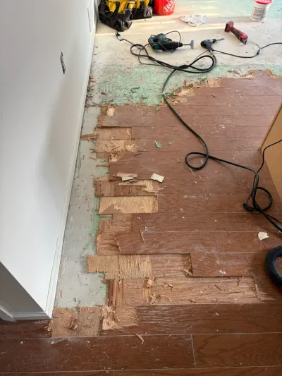 Partially removed wood flooring exposes plywood subfloor and tools during a renovation project.