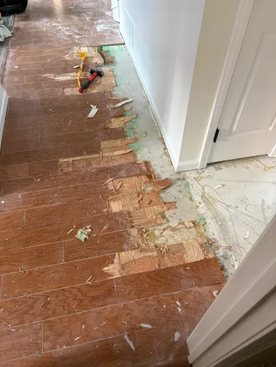 Hallway floor mid-demolition with wood planks torn up, exposing underlayment and concrete subfloor.