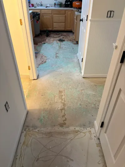 Hallway and kitchen with old flooring removed, exposing subfloor and adhesive residue during renovation.