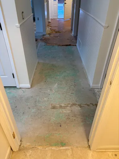 A hallway mid-renovation with old flooring removed, exposing subfloor and adhesive residue.