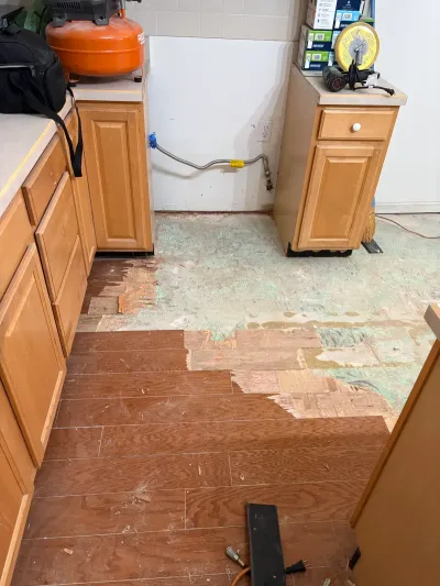 Kitchen under renovation with new plank flooring partially installed over exposed subfloor and tools on counters.