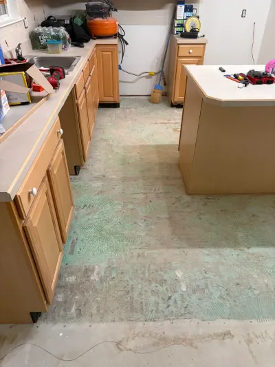 Kitchen mid-renovation with subfloor exposed, old oak cabinets intact, and tools scattered on counters.