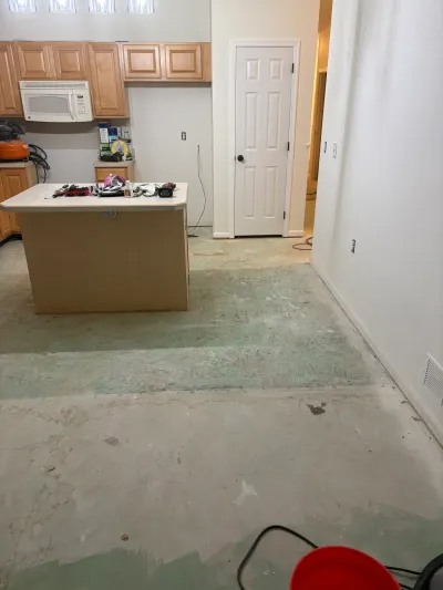 Kitchen mid-renovation with flooring removed down to subfloor, oak cabinets, and tools scattered about.