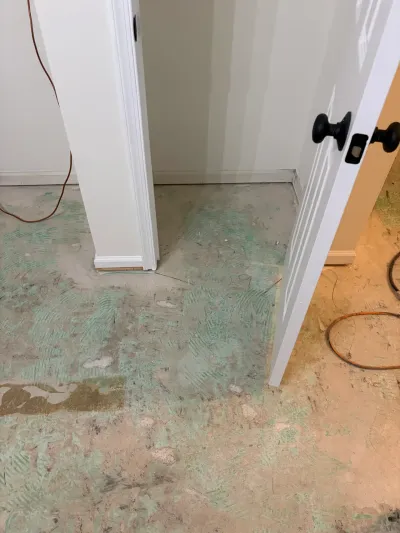 Bare subfloor with green adhesive residue and exposed wiring during a flooring demolition project.