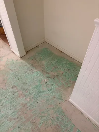 Concrete subfloor covered in dried green adhesive residue during a flooring demolition project.