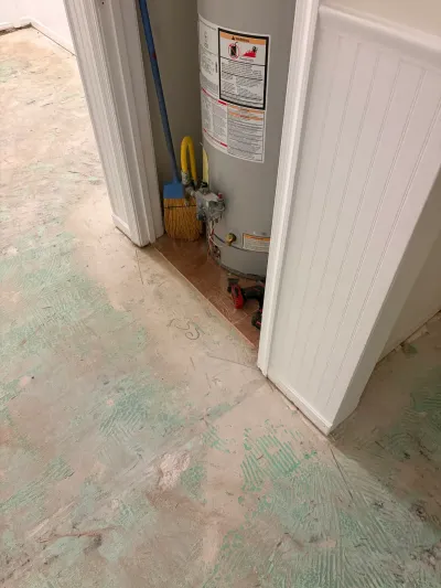 A water heater sits in a closet beside a hallway with subfloor exposed during a flooring renovation.