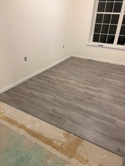 A room mid-renovation with new gray plank flooring meeting exposed subfloor and fresh white trim.